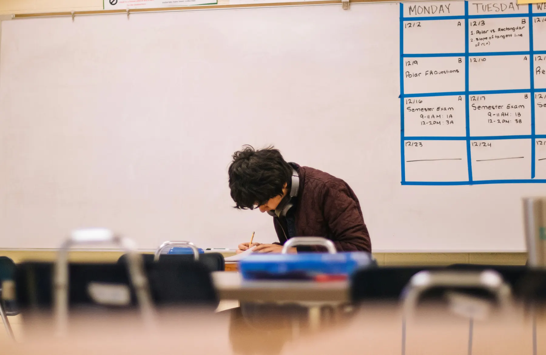 Student writing at a desk in front of a whiteboard