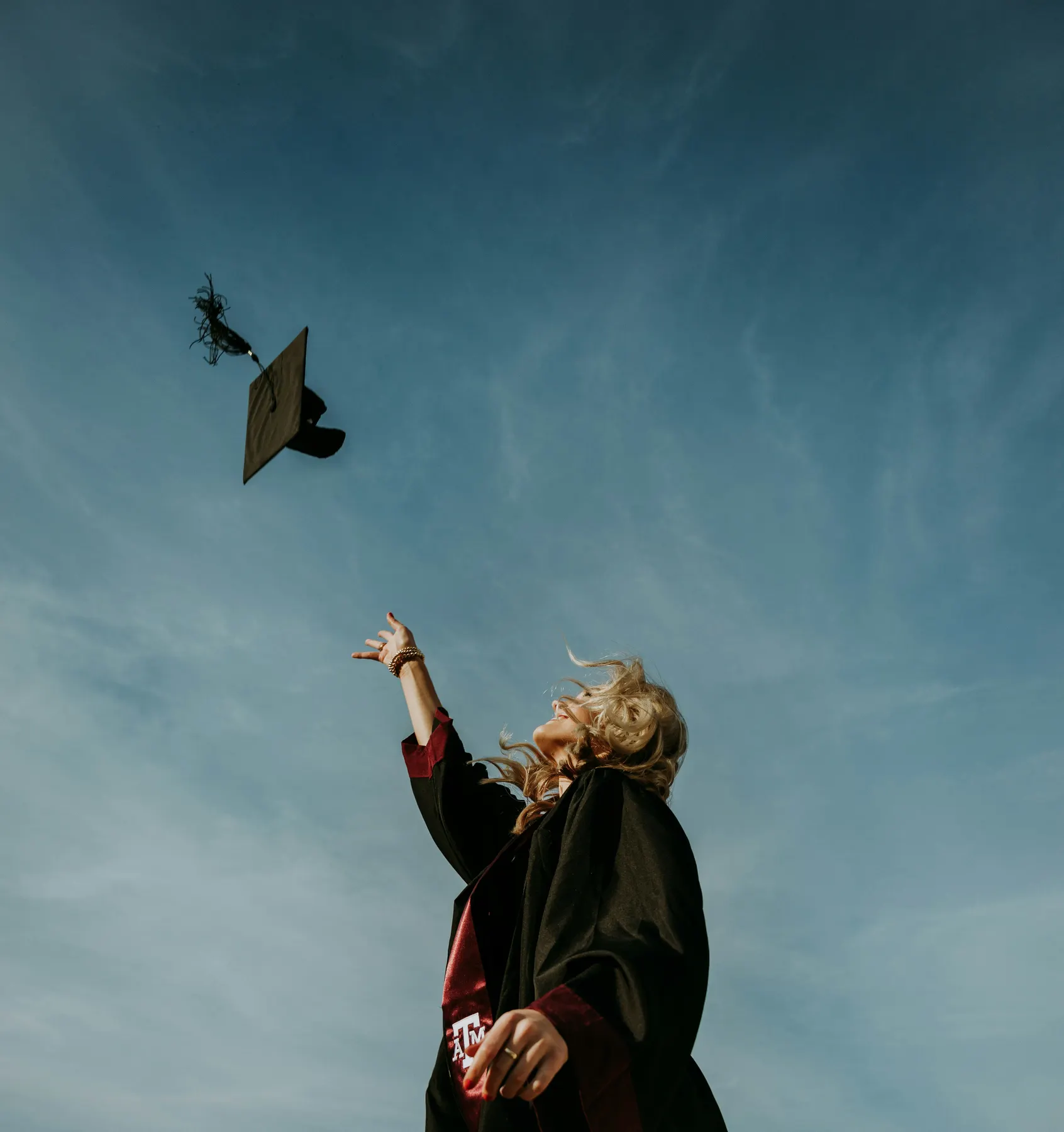 A graduate tossing a cap into a blue sky