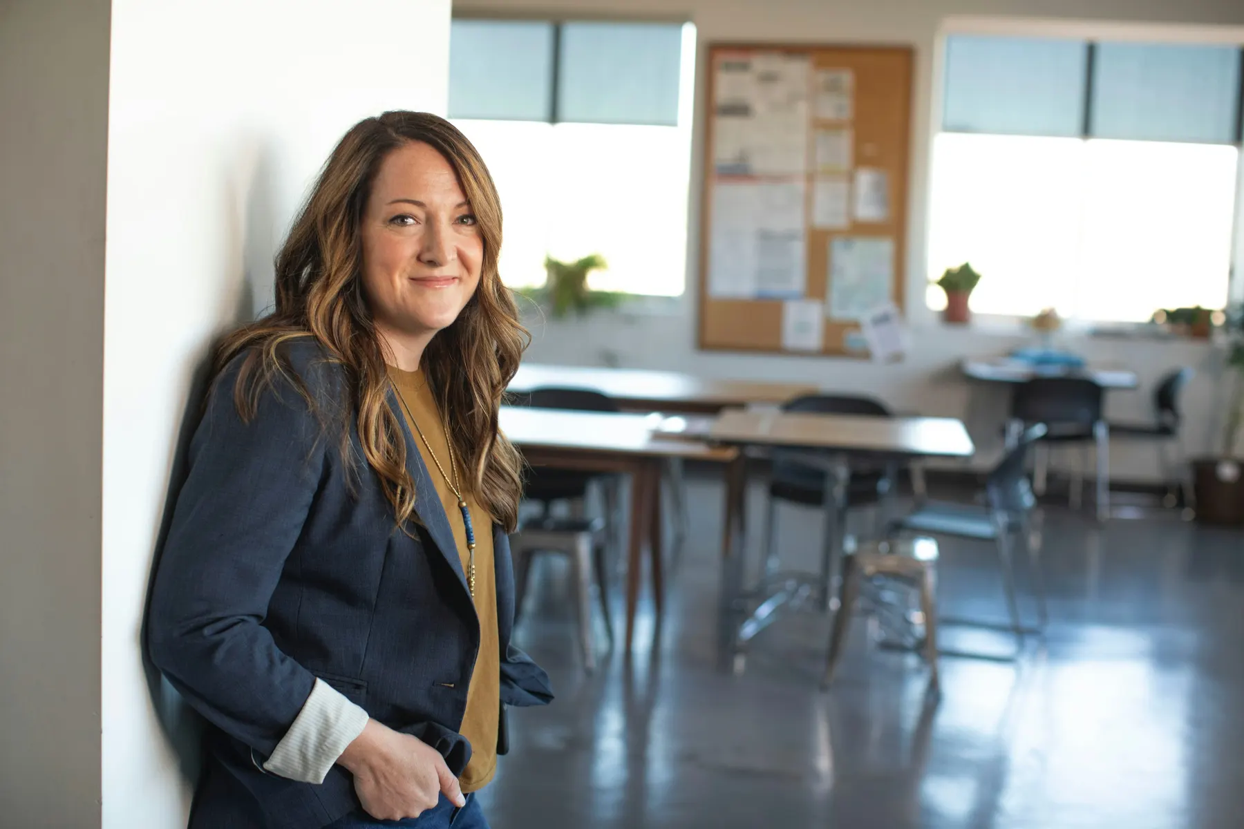 A smiling teacher leaning against a classroom wall