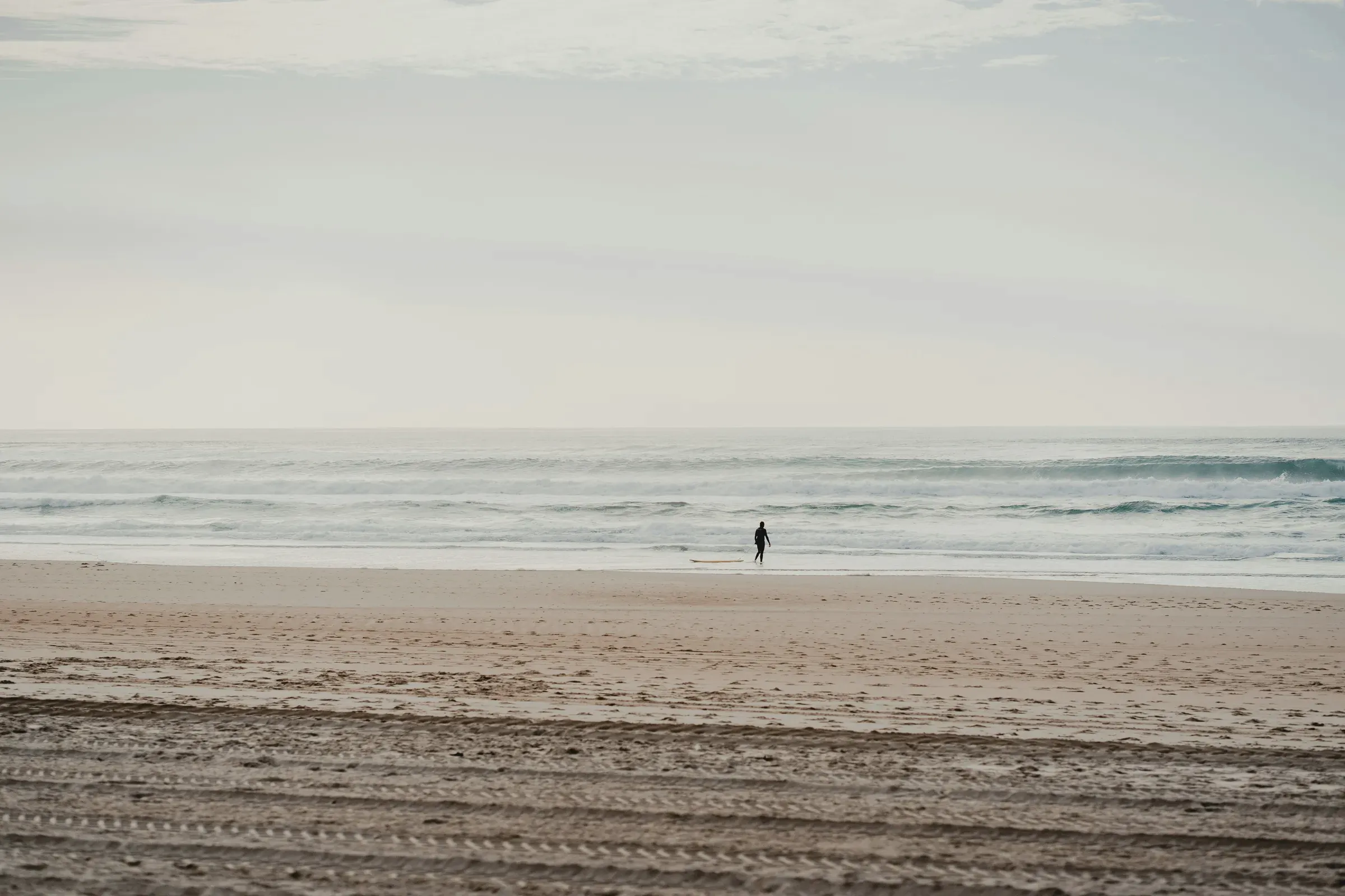 A wide beach with the swell running and one figure at the waterline