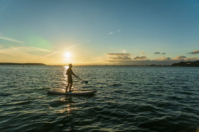 A paddleboarder crossing flat water at sunrise