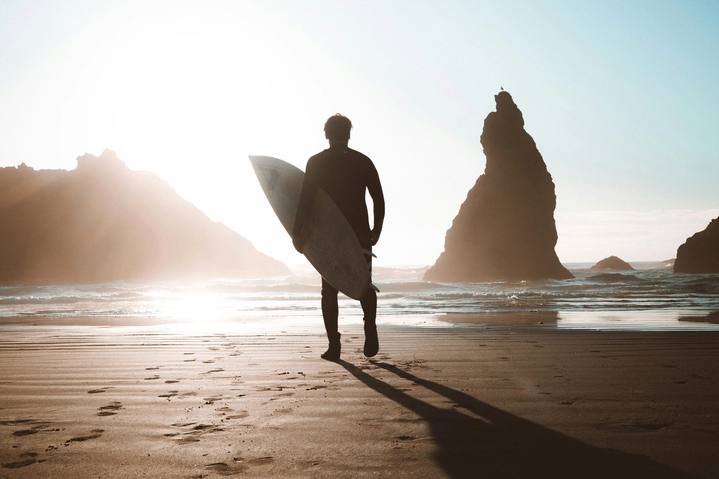 Surfer walking toward sea stacks at golden hour (placeholder photo)